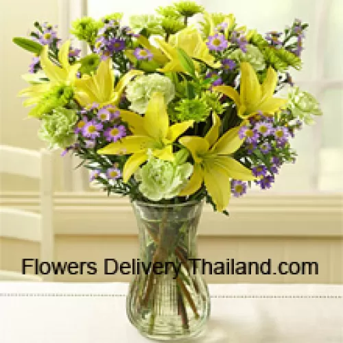 Lys jaunes et autres fleurs assorties disposées magnifiquement dans un vase en verre